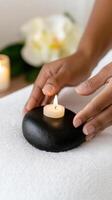 serene spa treatment featuring hand placing candle on smooth black stone, surrounded by soft towels and calming atmosphere photo