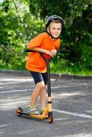 View of a young smiling boy an orange T-shirt on a scooter photo