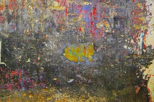 A vibrant abstract texture of a weathered wall with layers of peeling paint in red, yellow, and blue tones. photo