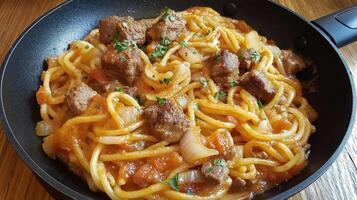 frying pan with a dish of spaghetti and meat. The spaghetti is cooked al dente and is topped with chunks of meat, onions, and a tomato sauce photo