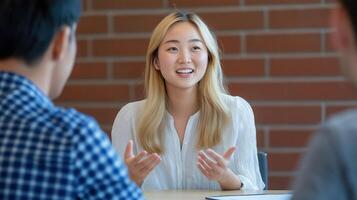asian young woman sitting at a table in a meeting with two men. She is smiling and appears to be engaged in a conversation with one of the men photo