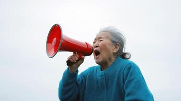 asian elderly woman, wearing a blue shirt, holding a red megaphone and shouting into it. She appears to be in the middle of a speech or shouting photo
