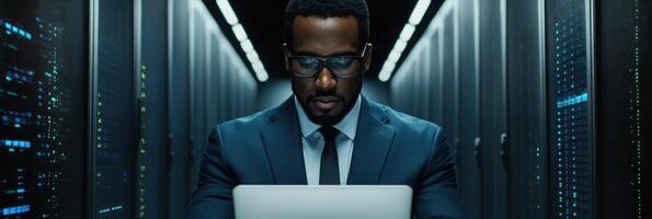 Man in formal attire focused on laptop in a modern server room with multiple servers around photo