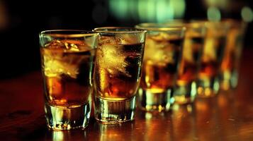 Several shot glasses filled with amber liquid and ice sit on a rustic bar counter, ready for serving photo
