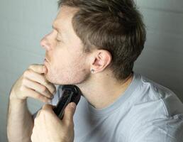 a man trims his beard with a trimmer. Close up. An electric razor trimming a beard. Beard care at home. photo
