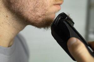 An electric razor trimming a beard. man trims his beard with a trimmer. photo
