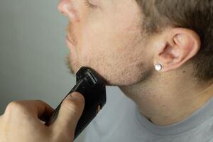 man trims his beard with a trimmer. An electric razor trimming a beard. Beard care at home. photo
