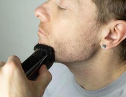 man trims his beard with a trimmer. electric razor trimming a beard. photo