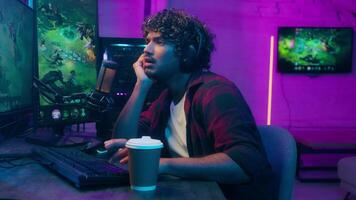 Sleepy bored Arabian Indian Latino man playing game cyber sport streamer gamer lazy guy drinking coffee tired male e-sport online computer home addict studio exhausted sleeping boredom streaming video
