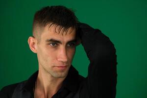 Young man in a green shirt with a concerned expression, holding his head in his hands, isolated over green background. photo