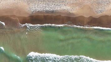 Antenne oben Aussicht von Strand und Ozean Wellen. Antenne Aussicht von ein sandig Strand mit sanft Ozean Wellen rollen auf zu das Ufer, Erstellen Muster im das Wasser und Sand. video