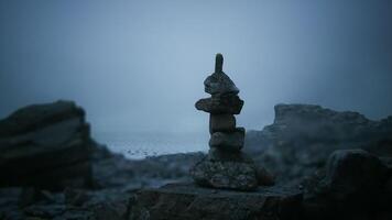 Rock stack balanced on a beach during foggy twilight hours near the ocean video