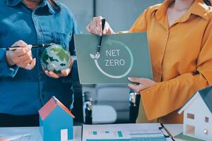 Two people holding a net zero sign and a house photo