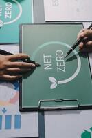 Two people are working on a green board with the word net zero photo