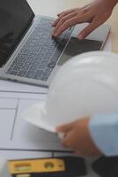 A person using a laptop on a table with a hardhat photo