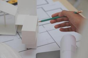 A person is holding a pencil and building model photo