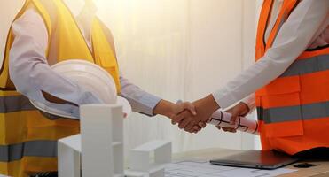 Two people shaking hands over a table with construction plans photo