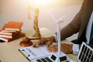 A man in a suit is writing on a legal document in front of a desk with a wind photo