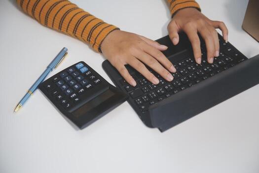 A person typing on a laptop with a calculator next to it photo