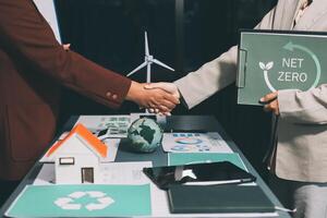 Two people shaking hands over a table with a net zero sign photo