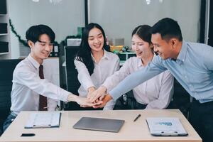 Asian business people holding hands together at desk photo