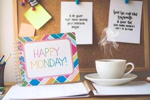 Happy monday colorful notebook with steaming cup of coffee and cork board with inspirational quotes photo