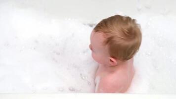 Little boy sitting in a bathtub with soap foam and soap bubbles video