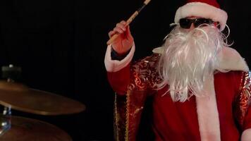 Santa claus wearing sunglasses and a fake beard energetically playing drums in a red and gold suit, creating a festive and unconventional christmas vibe in a dark setting video