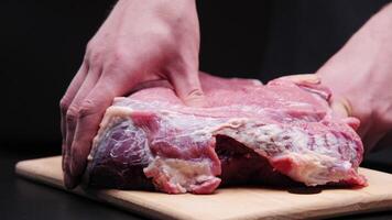 Male hands massaging a large beef steak on a black background. Preparing a tender beef steak for baking. Demonstration of the effect of massage on the body using a piece of meat as an example video