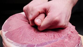 Male hands massaging a large beef steak on a black background. Preparing a tender beef steak for baking. Demonstration of the effect of massage on the body using a piece of meat as an example video