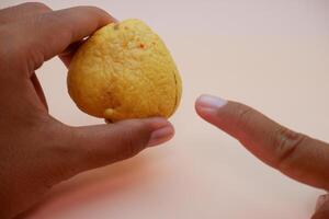 Close up of fingers holding an avocado pit with a soft orange backdrop photo