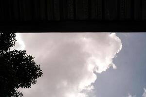 The blue sky is partially covered by the roof. One side shows a cloudy sky and the other side is covered by a roof. Low angle shot. Wallpapers Backgrounds. Negative Space. photo