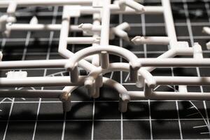 White Plastic Frames on Black rubber cutting mat. Abstract Backgrounds of model kit frames. Part of plastic model kit and tools for building robot. Miniature, Frame, Plastic, Object photo