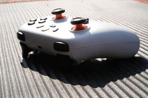 White game controller with a black striped background. The wireless gamepad has a dominant white color with orange on the joystick and black on each button. Game Controller isolated. Negative space photo