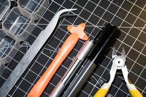 Set of hobby tools for building plastic model kits. Consisting of Nipper, Ink pen, cutting blade, plastic separator, tweezer, and transparent plastic container. Tools and equipments on black photo