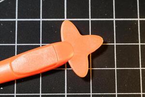 Closeup Orange Plastic opener on black striped rubber mat. Plastic opener is used to remove and disassemble model kits parts that have been installed. Plastic tools and equipment for hobbyists. photo