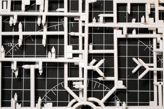 Stack of white Plastic Frames on Black rubber cutting mat. Abstract Backgrounds of model kit frames. Part of plastic model kit and tools for building robot. Miniature and Object photo