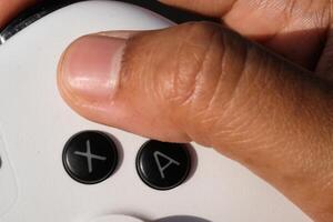 Thumbs are pressing buttons on a white gamepad. The game controller buttons are set soft and ergonomic. Finger mechanics and gameplay. Hobbies and leisures. Macrophotography Theme photo