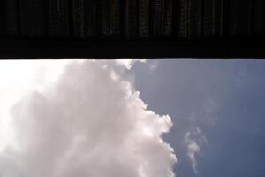 Backgrounds The blue sky is partially covered by the roof. One side shows a cloudy sky and the other side is covered by a roof. Low angle shot. Wallpapers Backgrounds. Negative Space. photo