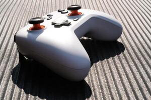 A Gamepad with a black striped background. The wireless gamepad has a dominant white color with orange on the joystick and black on each button. Game Controller isolated. Negative space photo