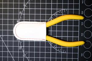 Closeup Yellow Nipper and white cap on black striped rubber cutting mat. Single blade nipper functions to cut plastic model kit parts. Metal tools for robot model kit hobbyists. photo