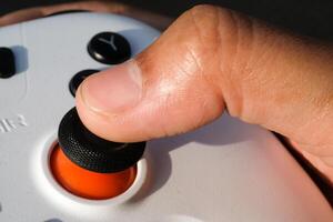 Thumbs are pressing buttons on a white gamepad. The game controller buttons are set soft and ergonomic. Finger mechanics and gameplay. Hobbies and leisures. Macrophotography photo