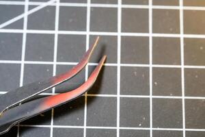 Metal precision tweezer with pointed tip. Tweezer is on a black cutting mat with lines. A tool that functions to clamp and pull out small objects. Negative Space photo