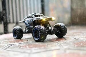 Toy car during outdoor rain with lights on. Remote Control Car being played in the yard during rain. Hobbies and Leisures. Toy Photography Concepts photo