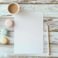 Blank paper, macarons and pencil on white wooden background photo
