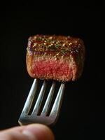 A hand holding a fork with a piece of steak on it photo