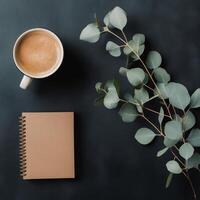 Coffee and notebook on a dark table with eucalyptus branch photo