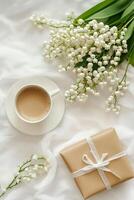 Cup of coffee and lily of the valley flowers on a white bed photo