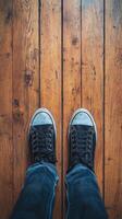 A person wearing black sneakers standing on a wooden floor photo