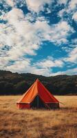An orange tent sits in a field with a blue sky photo